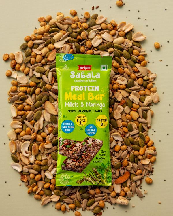 Millets & Moringa Meal Bar with seeds, almonds, and dates in green packaging surrounded by mixed nuts and seeds.