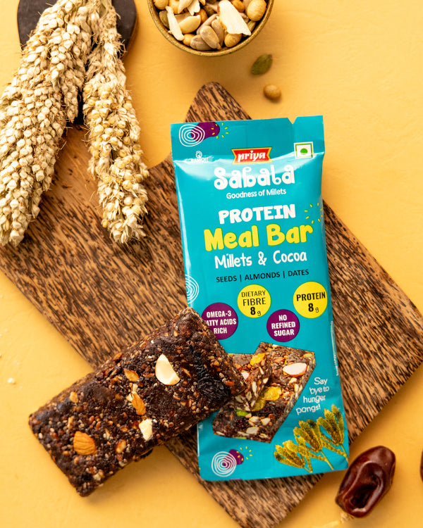 Millets & Cocoa Meal Bar protein snack with seeds, almonds, and dates on wooden board with millet grains and bowl of nuts