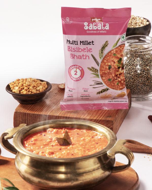 Multi Millet Bisibele Bhath in a traditional brass bowl with packaging and ingredients displayed around on a wooden surface