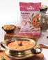 Multi Millet Bisibele Bhath in a traditional brass bowl with packaging and ingredients displayed around on a wooden surface