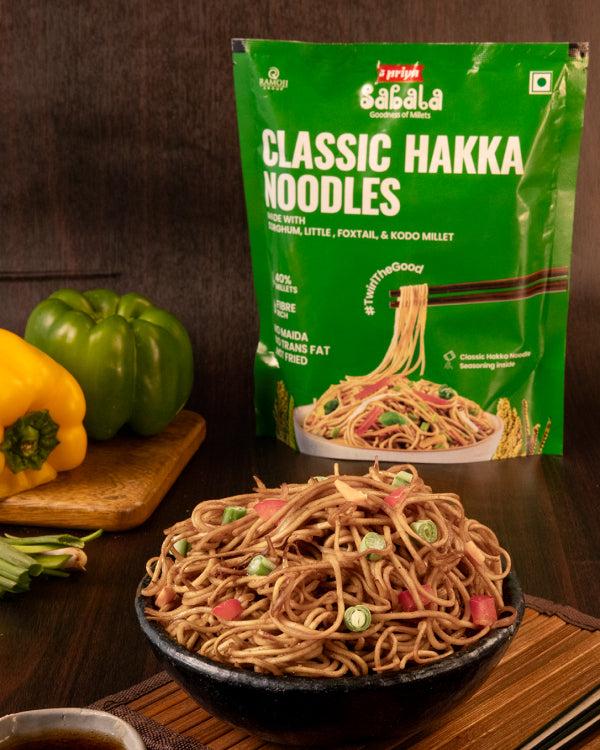 Millet Classic Hakka Noodles package with bowl of cooked noodles and fresh vegetables on wooden table