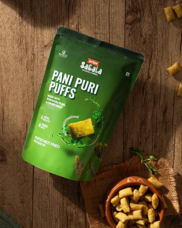 Green packaging of Pani Puri Puffs snack made with sorghum, pearl, and finger millet shown with bowl of crunchy puffs on wooden surface