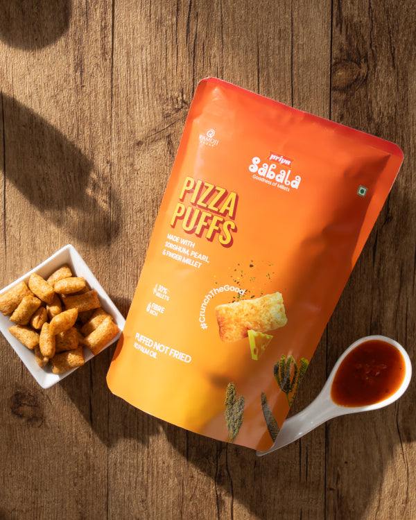 Crunchy baked Pizza Puffs snack with cheesy, tangy tomato and Italian herbs in orange packaging next to dipping sauce and bowl of puffs